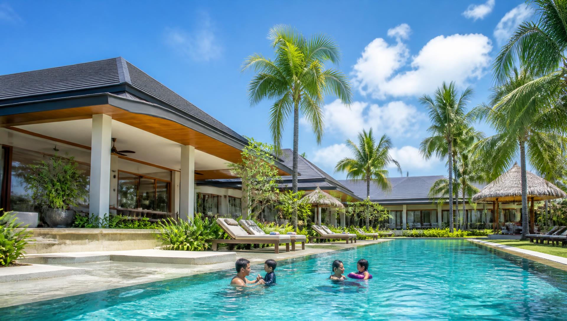 Uwina villas in daylight with a large tropical pool, palms and families enjoying the resort